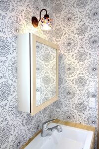 ステンドグラス風のライトが優しく照らす造作洗面台。花柄のアクセントクロスが清潔感のある空間を際立たせます。