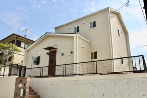 高台に建つ、ベージュの外壁と木調の玄関ドアが特徴的な2階建ての注文住宅