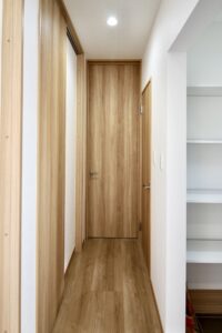 木目調の建具とフローリングが統一された廊下、正面にはLDKへ続く扉、右手にシューズクロークが見える玄関ホールの内観